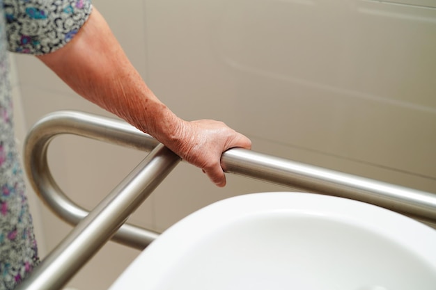 Asian elderly old woman patient use toilet support rail in bathroom bar security in nursing hospital