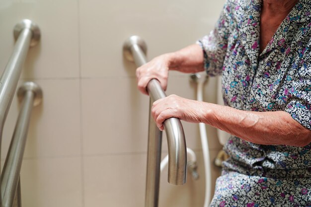 アジアの高齢の老婆患者は、看護病院でバスルームの手すりの安全手すりのセキュリティでトイレサポートレールを使用しています