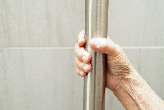 아시아 노인 여성 환자는 간호 병원의 욕실 손잡이 안전 손잡이 바 보안에서 변기 지지 레일을 사용합니다.