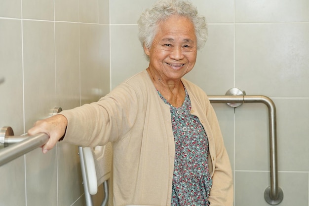 아시아 노인 여성 환자는 욕실 난간 안전 손잡이에서 변기 지지 레일을 사용합니다.
