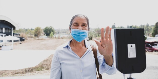 アジアの年配の観光客の女性は、熱温度スキャナー検出器の旅行の安全性で体温をチェックしました。