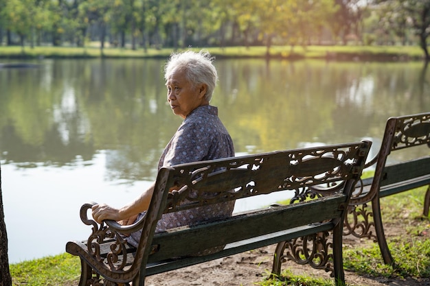 Asian elderly woman depressed and sad sitting back on bench in autumn park