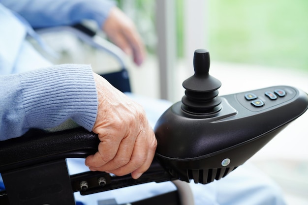 Asian elderly woman disability patient sitting on electric wheelchair in park medical concept