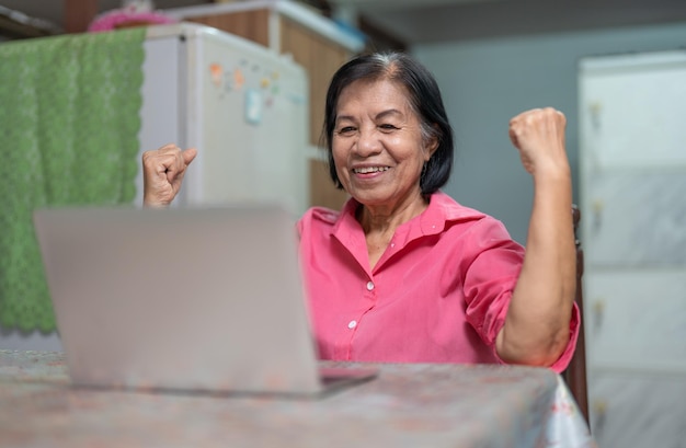 Asian elderly woman feeling glad and raising hand while talking with family in video conference