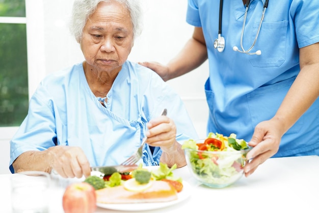 Asian elderly woman patient eating salmon stake and vegetable salad for healthy food in hospital