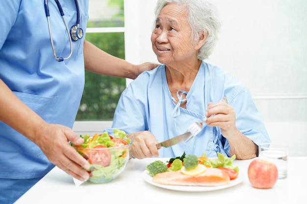 Asian elderly woman patient eating salmon stake and vegetable salad for healthy food in hospital