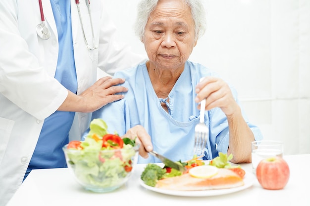 Asian elderly woman patient eating salmon stake and vegetable salad for healthy food in hospital