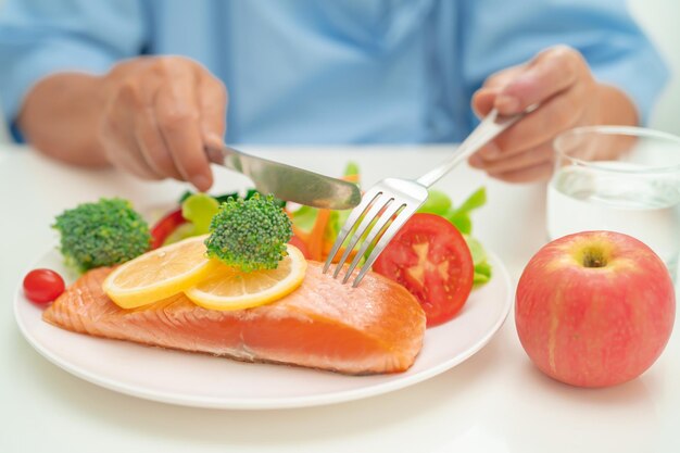 Пациент из Азии, пожилая женщина, ест завтрак из лосося и овощей в больнице.