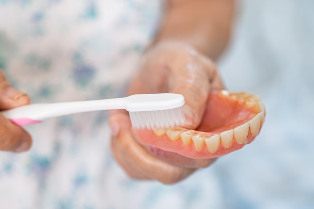 Asian elderly woman patient use toothbrush to clean partial denture of replacement teeth