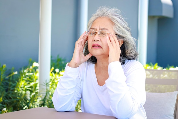 Asian elderly woman sitting in the garden outside the house She has a headache Health care concepts brain diseases of the elderly Retirement health insurance