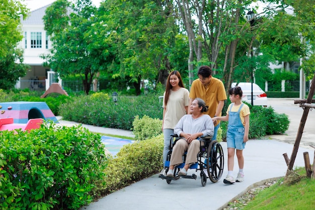 Donna anziana asiatica seduta su sedia a rotelle che passeggia con la sua famiglia felice quando cammina al parco verde