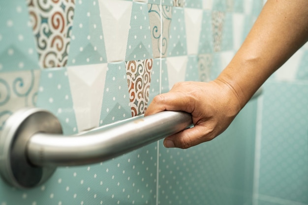 アジアの年配の女性は、トイレの健康的な強力な医療コンセプトでバスルーム ハンドル セキュリティを使用します。