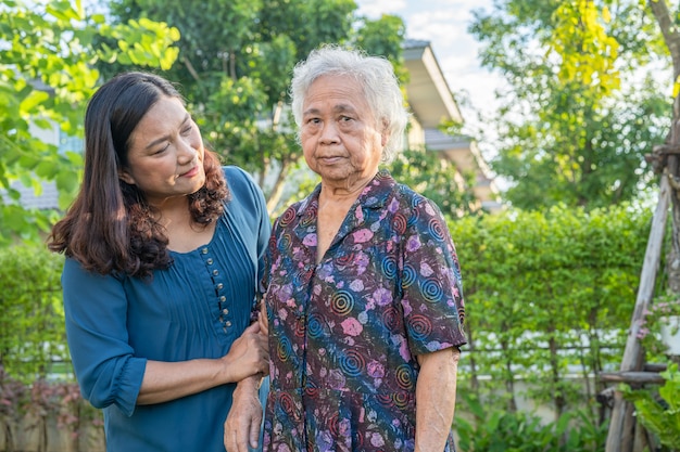 Asian elderly woman with caregiver walking with happy in nature park.