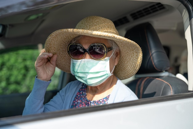 Asian elderly woman with mask and hat sitting in car with enjoy and freedom in traveling trip