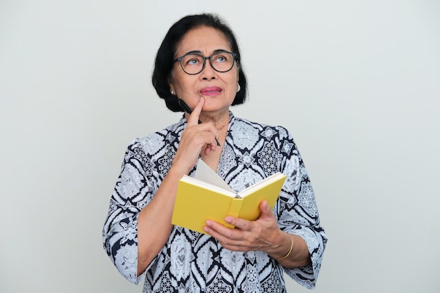Asian elderly women thinking about something while holding a book and pen