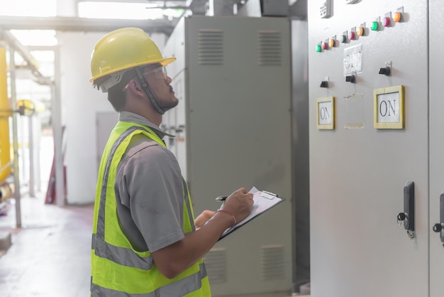 制御室の電気システムをチェックおよび監視するためのクリップボードを保持しているアジアの電気技師