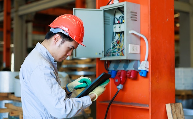 Asian Electrician engineer tests electrical installations on laptop and digital tablet computer at Heavy Industry Manufacturing Factory