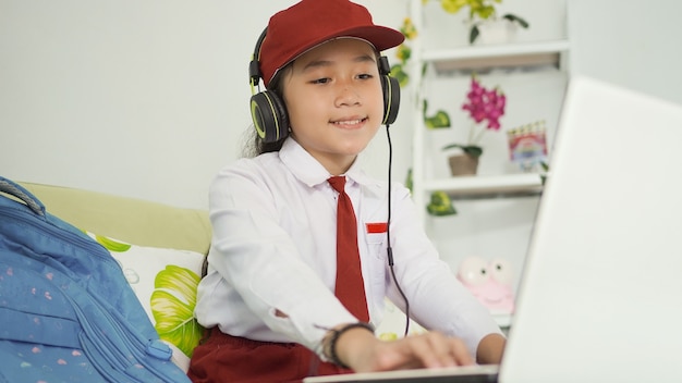 Asian elementary school girl studying online watching laptop screen at home