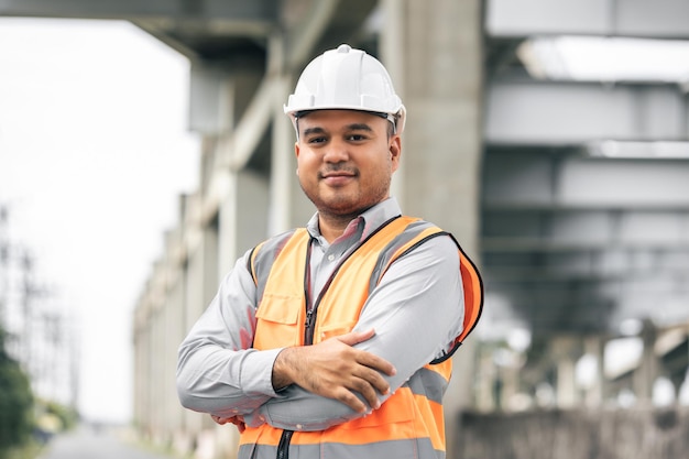 Photo asian engineer handsome man or architect looking construction with white safety helmet in construction site standing at highway concrete road site