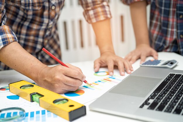 Foto l'ingegnere asiatico e il team di partner imparano e parlano con il grafico del progetto del piano della casa e il casco giallo e gli strumenti di costruzione ingegneristica sul lavoro al tavolo