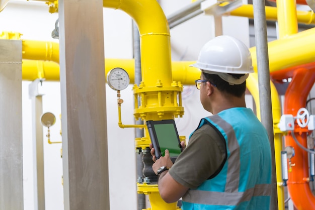 Asian engineer wearing glasses working in the boiler roommaintenance checking technical data of heating system equipmentThailand people