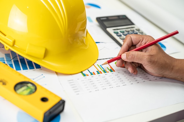 Asian engineer with plan project blueprint graph and yellow helmet and engineering construction tools