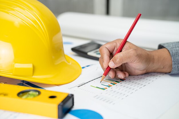 Asian engineer with plan project blueprint graph and yellow helmet