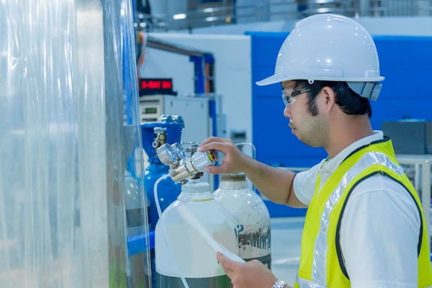 Asian engineer working at operating hallthailand people wear\
helmet workhe worked with diligence and patiencehe checked the\
valve regulator at the hydrogen tank