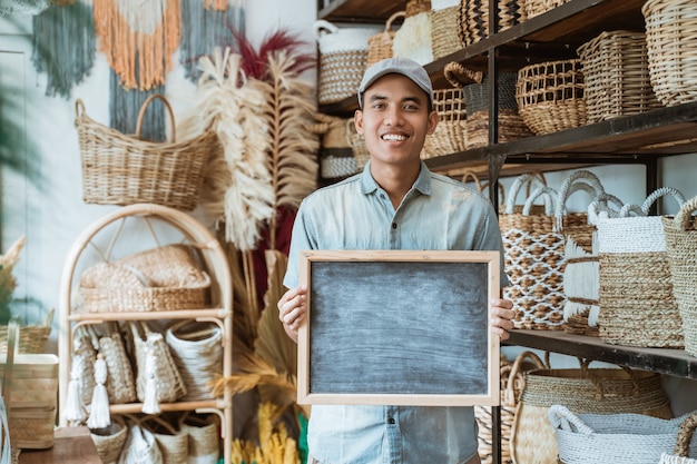 Asian entrepreneur holding a blackboard standing in a handicraft shop with a handicraft