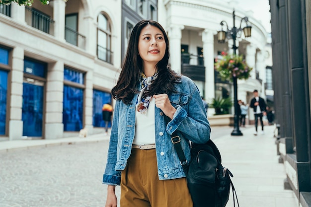 asian exchange student walking to school is appreciating the exotic buildings along the street. pretty young lady carrying backpack looking at distant view.