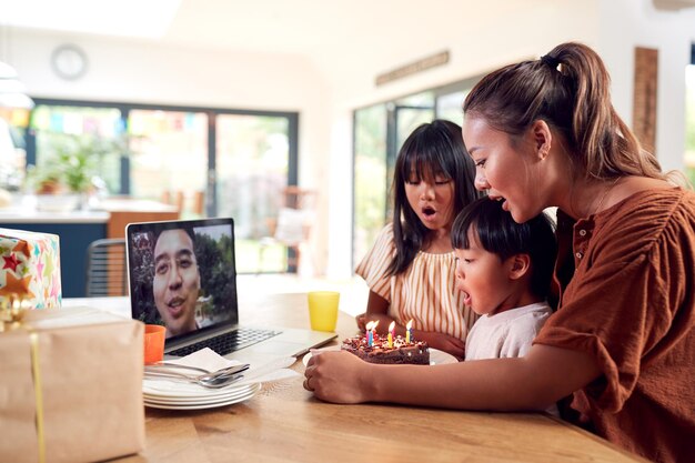 Asian Family Celebrating Birthday At Home With Father Working Away Via Video Call