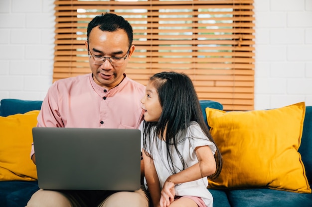 Photo an asian family enjoys quality time in their modern living room as the father works on his laptop and his daughter engages in elearning on a computer their bonding smiles and happiness are evident