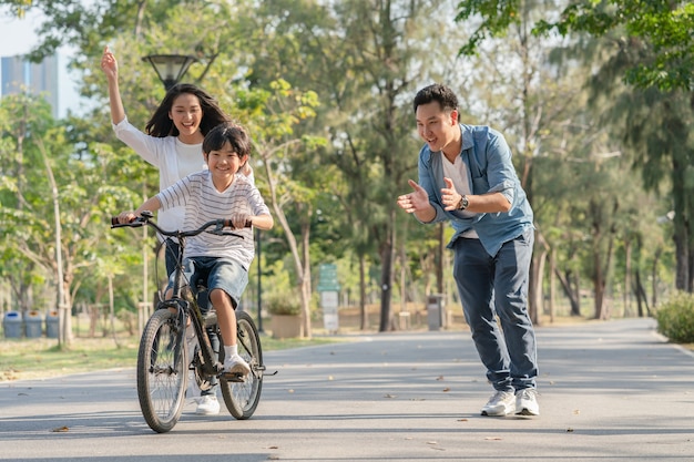 公園で自転車に乗ることを息子に教えるアジアの家族の父と母