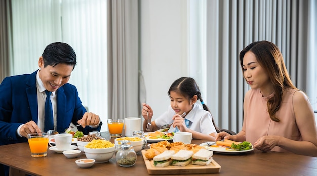 アジアの家族の父、父が仕事に出る前に家で朝一緒に食卓の台所で健康的な朝食用の食べ物を食べる子供の娘を持つ母、幸せな夫婦の大人の家族のコンセプト