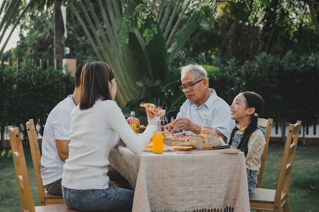 집에서 정원에서 피자를 먹는 아시아 가족. 뒤뜰에서 아이와 할아버지 생활 방식을 가진 부모.