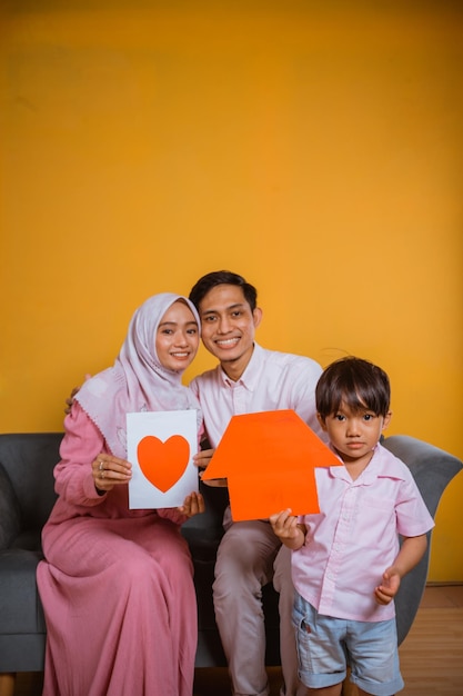 Asian family holding and showing a paper love drawing and paper home shapes when sitting on sofa