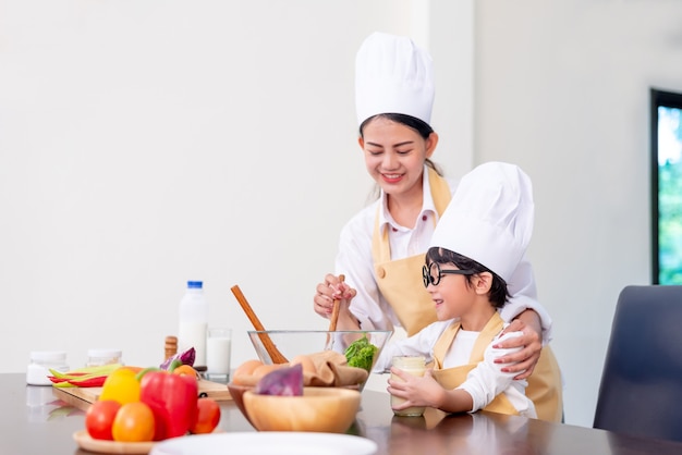 Asian family in the kitchen. Mom teaching son for cook healthy food in summer holiday.