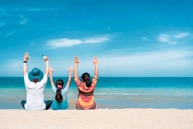 Asian family sitting relaxing on white sand beach with turqouise blue sea in sunny day, Summer trip concept