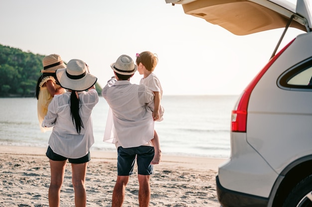 Vacanza in famiglia asiatica famiglia felice che corre sulla spiaggia al tramonto i genitori tenevano i figli e guardavano il tramonto dietro l'auto