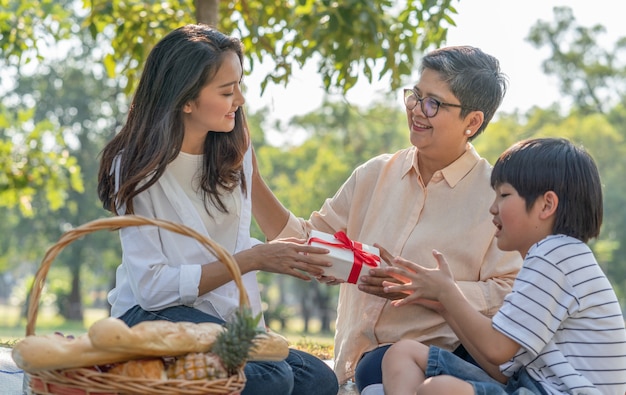 Asian family young woman giving gift box to grandmother while picnicking in the park