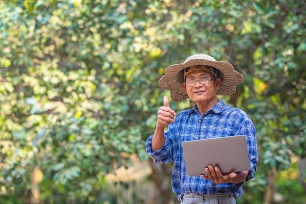 Coltivatore asiatico nel campo con il computer portatile