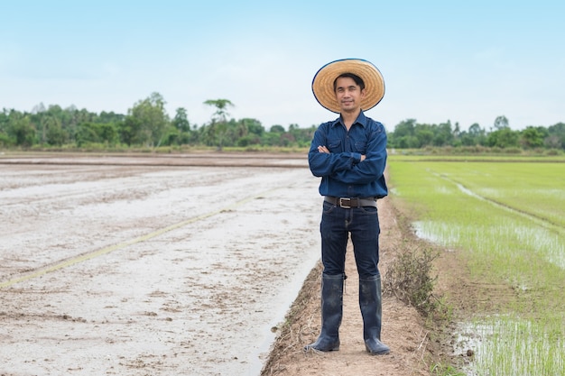 Asian farmer man wear blue shirt and hat stand with cross arm at green rice farm.