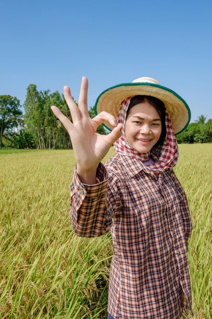 Donna contadina asiatica che indossa un turbante in piedi con la mano giusta con un volto sorridente in mezzo al campo
