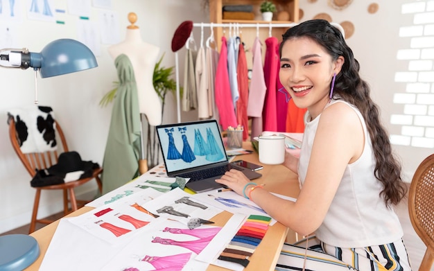 asian Fashion designer drawing sketches for new collection on computer laptop