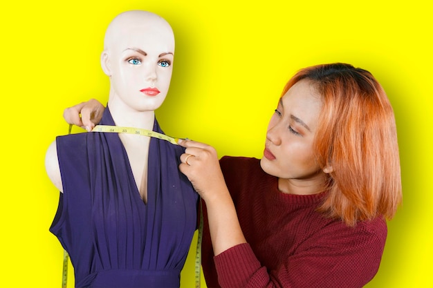 Asian fashion designer measuring mannequin neck with measuring tape isolated over yellow background