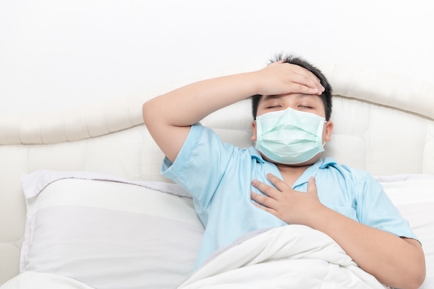 Asian fat boy wear surgical mask with a high fever and chest pain on bed,