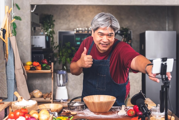 Un uomo grasso asiatico in piedi in cucina a preparare l'attrezzatura per realizzare contenuti sulla pizza fatta in casa