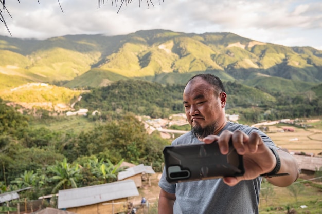 Азиатский толстый путешественник делает селфи с прекрасным видом на горы деревни Сапан в Нан ТаиландСапан - маленькая и спокойная деревня в горах Таиланд