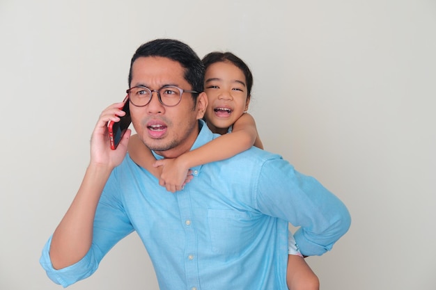 Asian father carry his daughter in the back while answering a phone call
