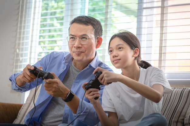 Asian father and daughter playing video games at home People doing activities and family concepts